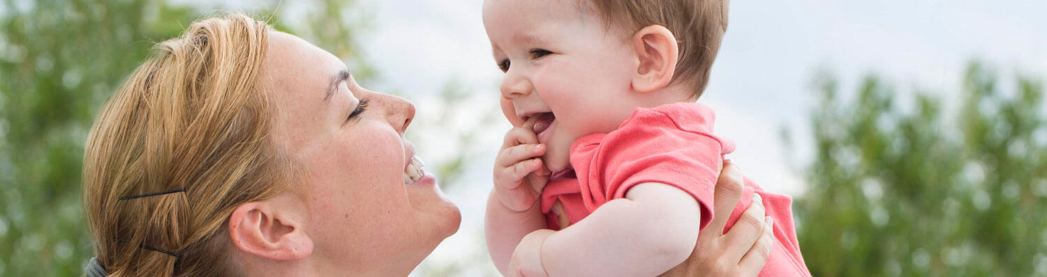A woman holds a baby outdoors.