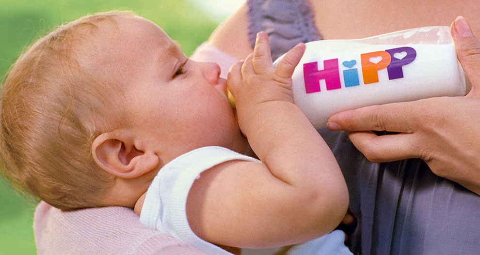 A baby drinks from a bottle with the word "HiPP" on it.
