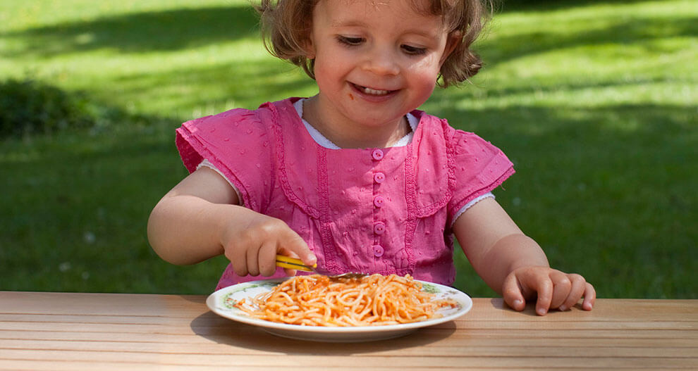 A child in a pink shirt is eating spaghetti from a white plate.