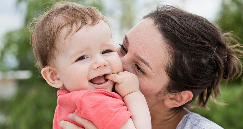 A woman lovingly holds a baby outdoors.