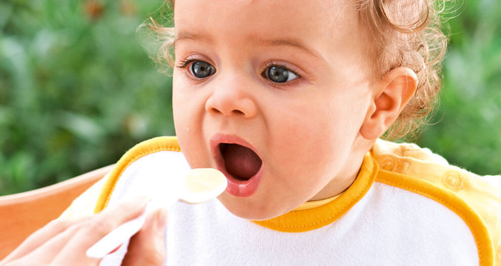 A baby with curly hair is being fed with a spoon.