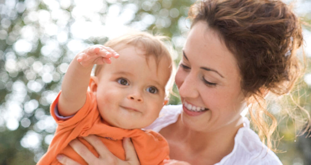 A woman holds a baby outdoors.