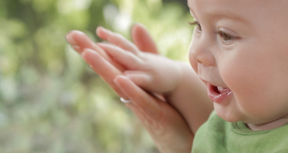 Baby in green shirt, looking to the side, with a blurred green background.