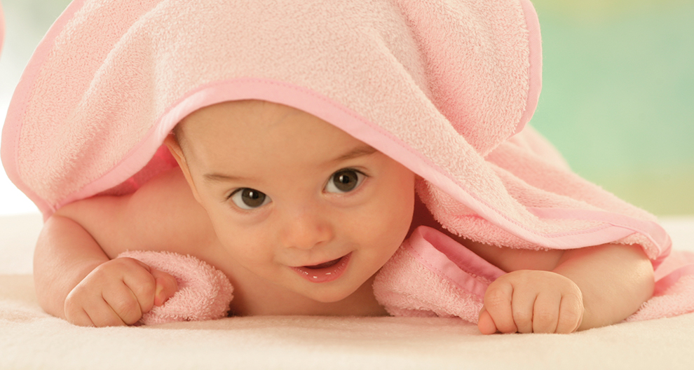 Baby wrapped in pink towel, looking curious.