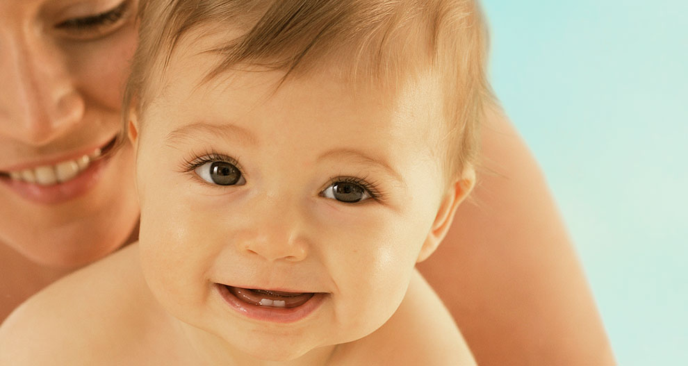 A close-up of a baby's face with a partial view of an adult's face in the background.
