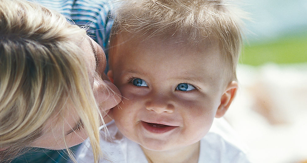 A woman is kissing a baby on the cheek.