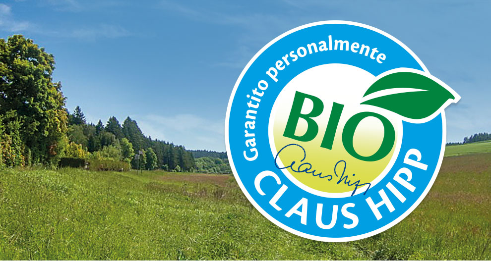Un paesaggio con erba verde e alberi è sovrapposto a un logo circolare blu con la scritta "BIO" in bianco, "Garanito personalmente" in verde e "Claus Hipp" in bianco.