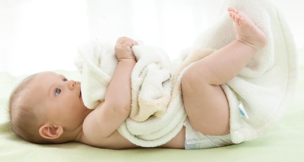 Un bambino giace su una superficie verde, avvolto in un asciugamano bianco, con un pannolino visibile.