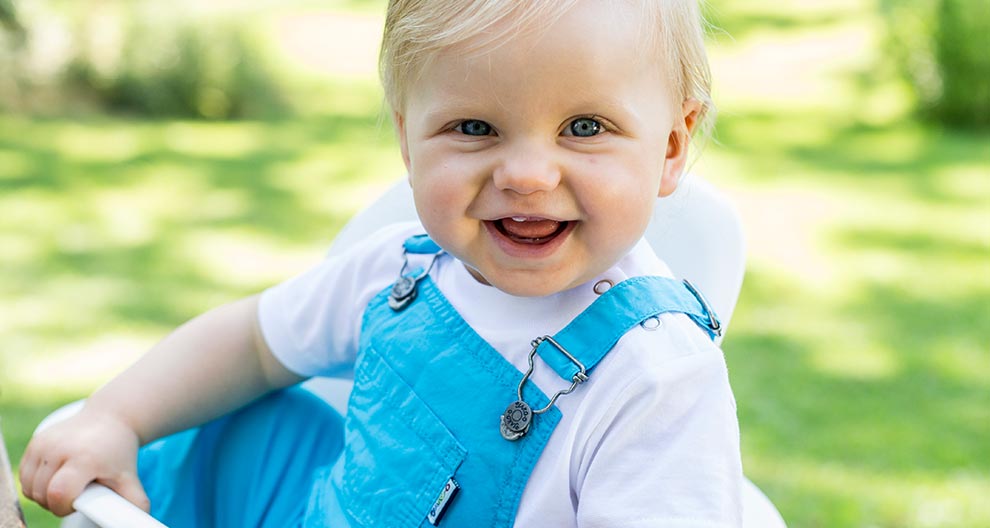 Un bambino in tuta blu siede all'aperto, tenendo in mano un oggetto bianco.